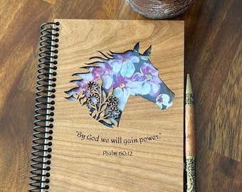Puede incluir: Un diario de madera con un diseño floral recortado en la portada. El diario tiene una encuadernación en espiral negra y presenta la cita "By God we will gain power." Salmo 60:12.