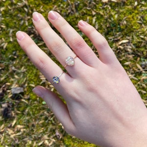 Pu&ograve; includere: Due anelli d'oro con bande delicate e montature in resina ovali. L'anello pi&ugrave; grande presenta un motivo floreale bianco, mentre l'anello pi&ugrave; piccolo ha un motivo floreale blu e giallo.