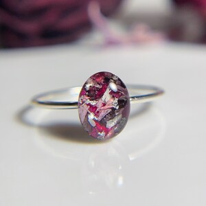 Pu&ograve; includere: Un anello d'argento con una pietra ovale in resina rosa e viola. La pietra &egrave; piena di piccoli pezzi di fiori secchi e scaglie d'argento.