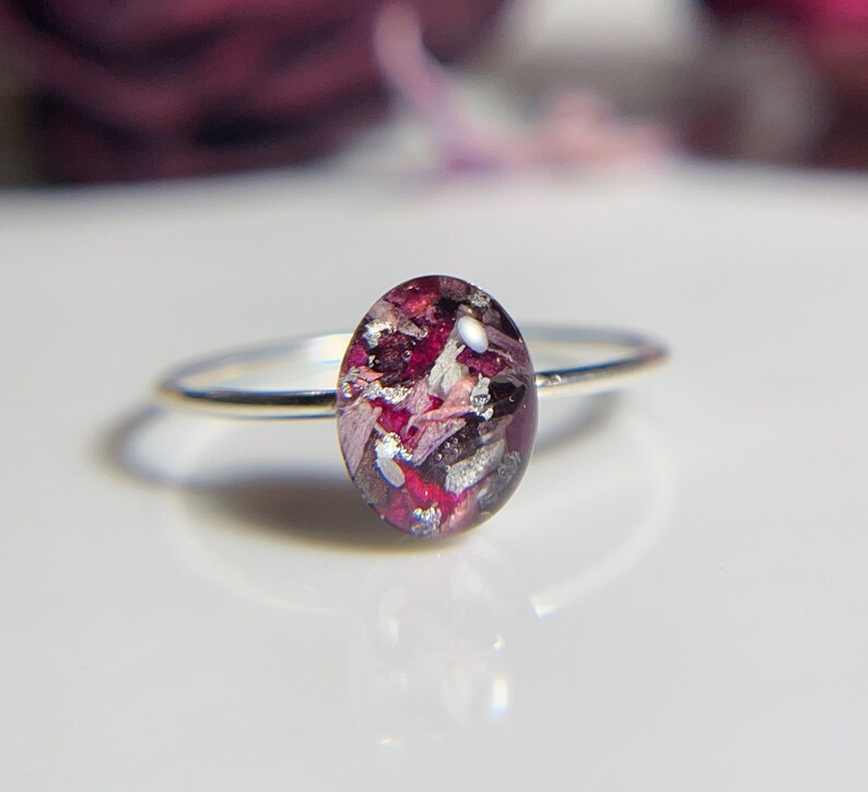 Pu&ograve; includere: Un anello d'argento con una pietra ovale in resina rosa e viola. La pietra &egrave; piena di piccoli pezzi di fiori secchi e scaglie d'argento.