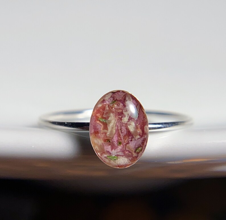 Pu&ograve; includere: Un anello d'argento con una pietra ovale in resina rosa e bianca. La pietra &egrave; piena di piccoli pezzi di fiori secchi.