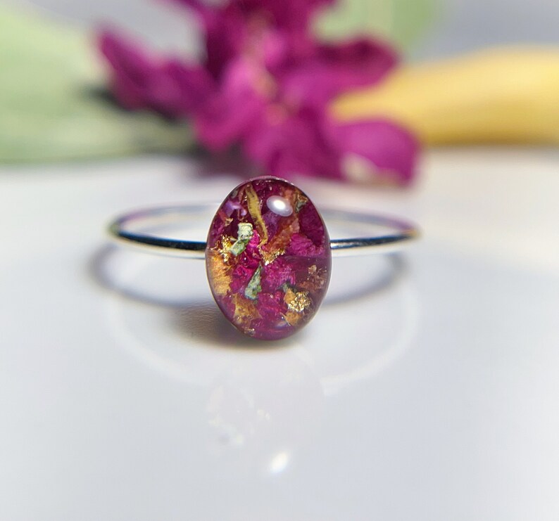 Pu&ograve; includere: Un anello d'argento con una montatura rotonda in resina trasparente che contiene fiori rosa e dorati pressati.