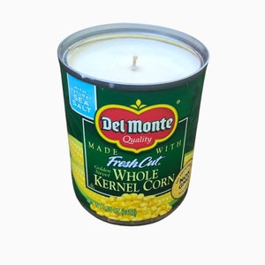 Puede incluir: Una vela de la marca Del Monte en una lata con forma de lata de maíz. La vela es blanca y tiene una etiqueta verde con las palabras "Del Monte Quality" y "Fresh Cut Golden Sweet Whole Kernel Corn" impresas en ella. La lata es de 6,75 onzas (248 g).