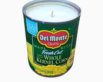 May include: A Del Monte brand candle in a can shaped like a can of corn. The candle is white and has a green label with the words "Del Monte Quality" and "Fresh Cut Golden Sweet Whole Kernel Corn" printed on it. The can is 6.75 ounces (248g).