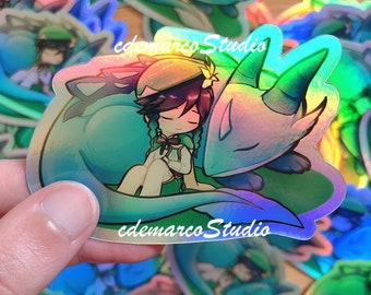 May include: A holographic sticker featuring a cartoon character with purple hair wearing a green hat and a green dress, holding a blue and green dragon. The sticker has the text "edemarcoStudio" printed on it.