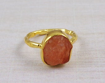 May include: A gold ring with a large, rough-cut, orange gemstone. The ring has a textured band.
