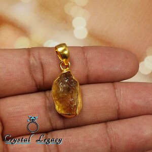 Pu&ograve; includere: Ciondolo dorato con una pietra di citrino grezza color ambra. Il ciondolo ha un design semplice con un'ansa dorata per attaccarlo a una catena. La gemma &egrave; di forma irregolare, mostrando la sua forma naturale. Gioiello.