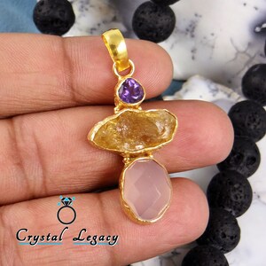 May include: Gold pendant featuring three raw gemstones: a purple amethyst, a yellow citrine, and a pink rose quartz.