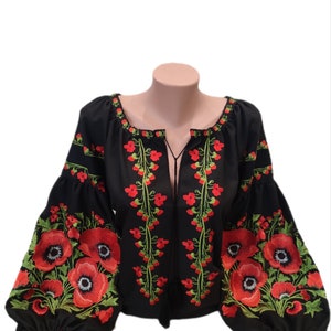 May include: Black blouse with red poppy embroidery. The blouse has long, puffed sleeves and a floral design around the neckline and front. The poppies have green leaves and stems.