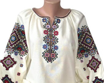 May include: A white embroidered blouse with a V-neck and long sleeves. The embroidery is in a geometric pattern with red, blue, green, and yellow colors.