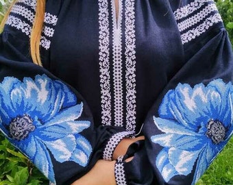 Op de afbeelding: Een zwarte geborduurde blouse met witte en blauwe bloemenmotieven. De blouse heeft een ronde hals en lange mouwen.
