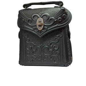 May include: A black leather handbag with intricate embossed floral designs and a brass clasp. The bag has a short handle and a flap closure.