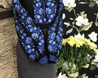 Op de afbeelding: Een zwarte geborduurde blouse met blauwe bloemenpatronen. De blouse heeft lange mouwen en een ronde hals.