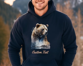 May include: Navy blue hoodie featuring a watercolor illustration of a grizzly bear. The bear is brown and tan, with a detailed depiction of its fur. The hoodie has a front pocket and the text "Custom Text" at the bottom.