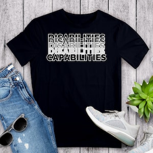 May include: Black t-shirt with the text "DISABILITIES" repeated four times in a gradient pattern, with the last line reading "CAPABILITIES".