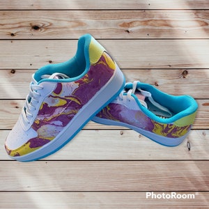 May include: A pair of white canvas sneakers with a blue trim and a marbled design in shades of yellow, pink, and purple.