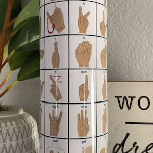 May include: White tumbler with a graphic of American Sign Language letters and numbers. The letters include b, c, j, k, r, s, z, and the numbers include one, nine, and eight. The words love, yes, and no are also included.