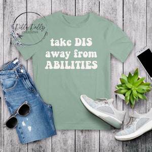 May include: A sage green t-shirt with the text "take DIS away from ABILITIES" in white retro-style lettering.
