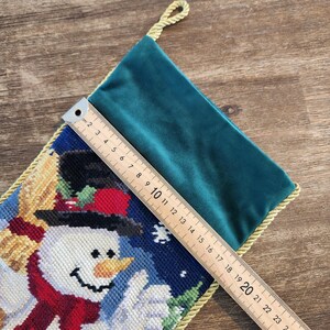 K&ouml;nnte beinhalten: Ein gr&uuml;ner Samtstrumpf mit einem Schneemann-Motiv. Der Strumpf ist mit goldener Kordel verziert und hat eine Schlaufe oben. Der Schneemann tr&auml;gt einen roten Schal und einen schwarzen Zylinder. Der Strumpf ist 51 cm lang.