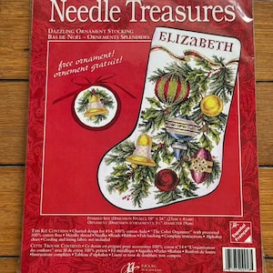 May include: A Needle Treasures cross stitch kit for a Dazzling Ornament Stocking featuring the name Elizabeth. The packaging displays a finished stocking with ornaments and greenery, a free ornament design, and lists a finished size of 25 cm by 41 cm.