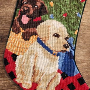 Może przedstawiać: Choinka świąteczna z czerwono-czarną kratą, przedstawiająca dwa psy. Jeden pies to brązowy labrador retriever, a drugi to ż&oacute;łty labrador retriever. Psy siedzą przed zielonym drzewem bożonarodzeniowym z lampkami.
