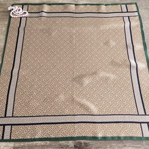 May include: A tan and cream-colored silk scarf with a geometric pattern. The scarf has a dark green border and black and cream-colored trim. A string of pearls is in the upper left corner. The scarf is approximately 28 inches square.