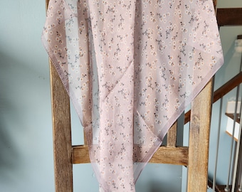 May include: A light pink sheer scarf with a small white floral pattern. The scarf is draped over a wooden chair.