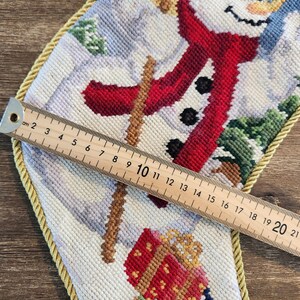 K&ouml;nnte beinhalten: Ein wei&szlig;er Strumpf mit einem Schneemann-Motiv. Der Schneemann tr&auml;gt einen roten Schal und einen schwarzen Hut. Der Strumpf ist mit einer goldenen Kordel verziert. Der Strumpf ist 50,8 cm lang.