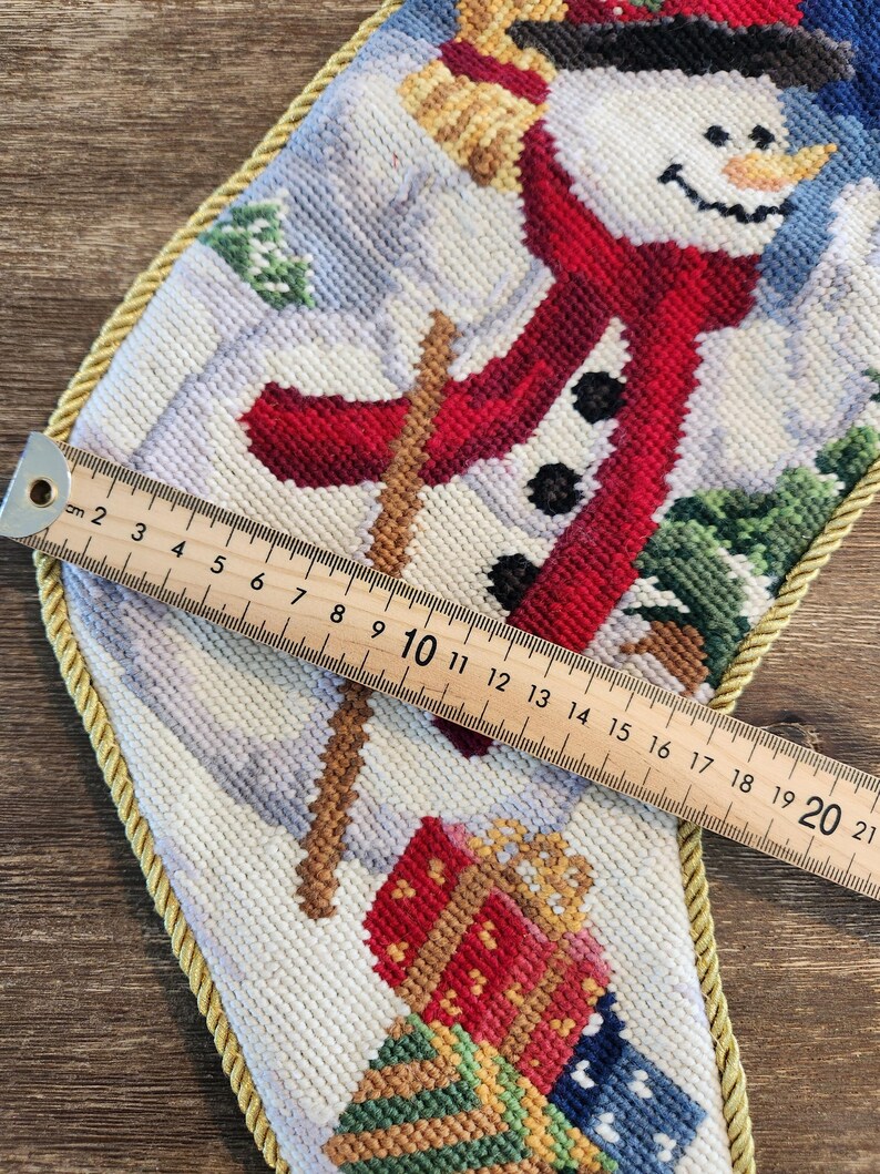 K&ouml;nnte beinhalten: Ein wei&szlig;er Strumpf mit einem Schneemann-Motiv. Der Schneemann tr&auml;gt einen roten Schal und einen schwarzen Hut. Der Strumpf ist mit einer goldenen Kordel verziert. Der Strumpf ist 50,8 cm lang.