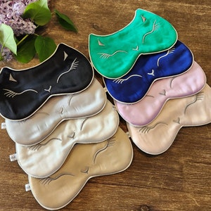 May include: A stack of six sleep masks featuring a cat face design. The masks are made from silk and come in a range of colours, including black, green, blue, pink, and beige.