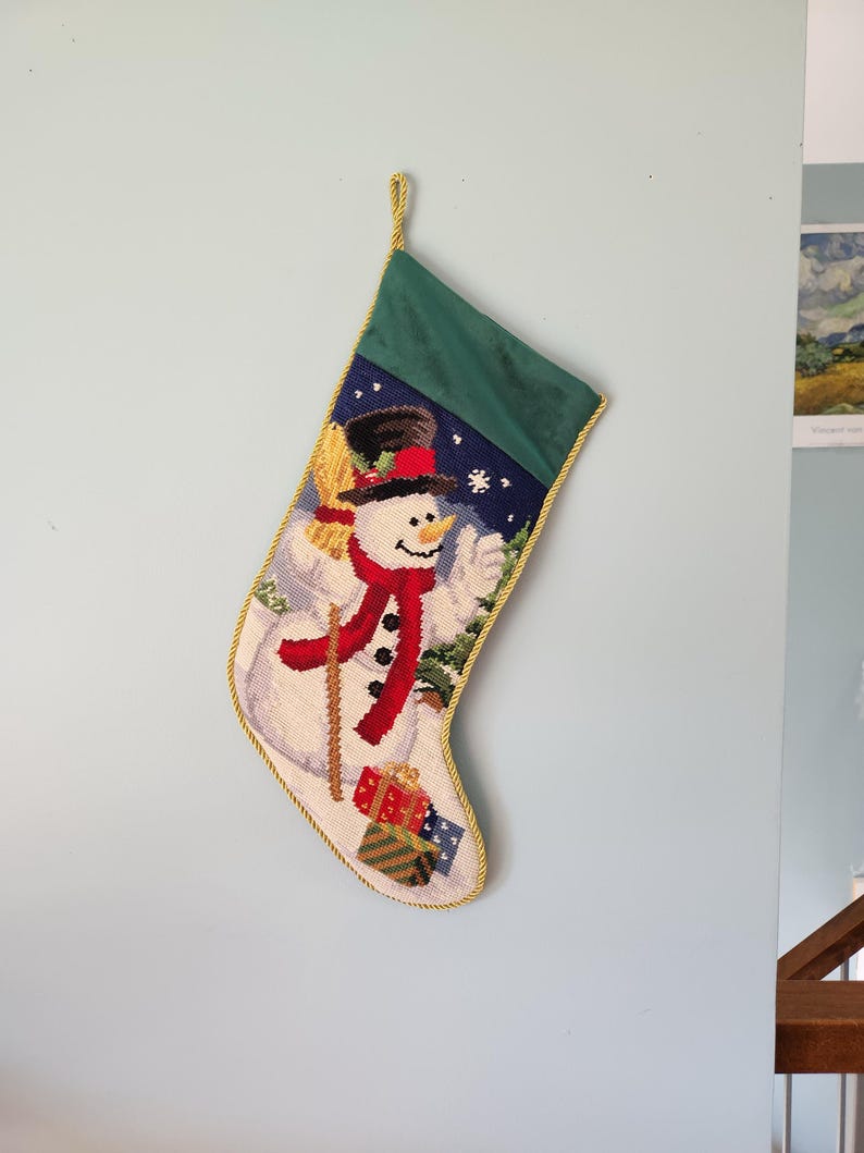 K&ouml;nnte beinhalten: Ein gr&uuml;ner und wei&szlig;er Weihnachtsstrumpf mit einem Schneemann, der einen Besen und Geschenke h&auml;lt. Der Strumpf hat einen goldenen Besatz.