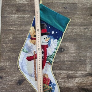 K&ouml;nnte beinhalten: Ein wei&szlig;er Weihnachtssocken mit einem Schneemann-Motiv. Der Socken ist mit goldener Litze verziert und hat einen gr&uuml;nen Samt-Manschetten. Der Schneemann tr&auml;gt einen roten Schal und Hut und h&auml;lt ein Geschenk. Der Socken ist 142 cm lang.