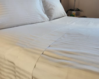 May include: White striped bed sheets with two white pillows on a wooden bed frame.