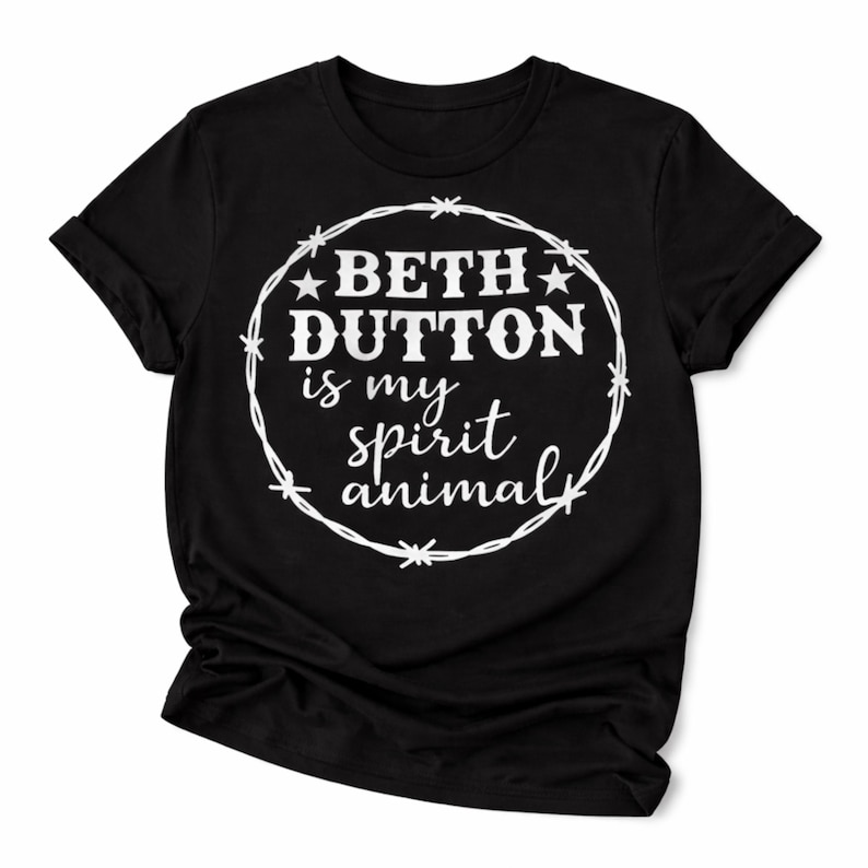 May include: Black t-shirt with the text "BETH DUTTON is my spirit animal" in a white, circular design. The design includes stars and a barbed wire-like border. The shirt is made of a soft material and has rolled-up sleeves.