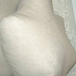 May include: Two beige fabric dress forms, designed in a bust shape. The forms are made of a textured fabric, with visible seams. The forms are positioned against a white lace background.
