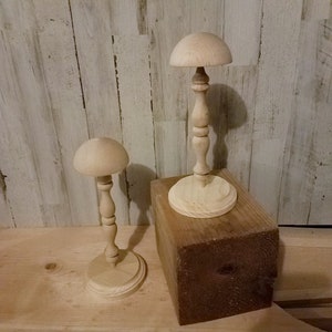 May include: Two wooden hat forms on stands. The larger form is on a wooden block. Both forms are made of natural wood.