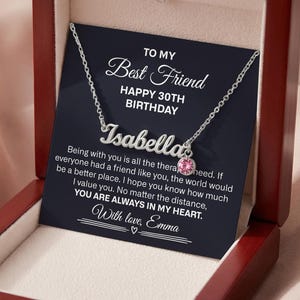 May include: A silver necklace with the name "Isabella" in cursive script, presented in a wooden gift box. The necklace features a pink gemstone pendant. A card inside reads "To My Best Friend, Happy 30th Birthday."