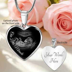 Peut inclure: Un collier pendentif argenté en forme de cœur. Le recto présente une image échographique en niveaux de gris avec le texte "Our Little Miracle". Le verso est vierge avec le texte "Your Words Here".