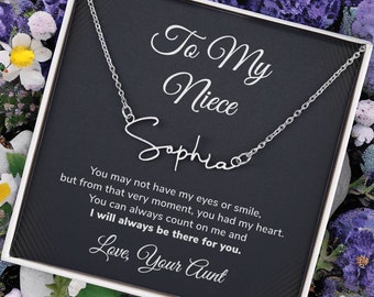 May include: A silver necklace with a cursive name pendant that reads "Sophia" in a black gift box with a message that reads "To My Niece Sophia You may not have my eyes or smile, but from that very moment, you had my heart. You can always count on me and I will always be there for you. Love, Your Aunt"