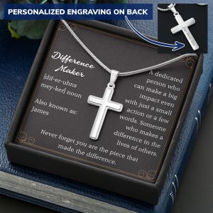 May include: A silver cross pendant on a chain, presented in a black gift box. The cross is the focal point, with a white border. The box contains text that reads "Difference Maker" and "Never forget you are the piece that made the difference."