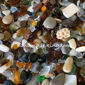 May include: A close-up image of a variety of sea glass and beach pebbles in shades of brown, white, gray, green, and orange. The sea glass is smooth and polished, while the pebbles are rough and textured. The image includes the text "handmade kingdom".