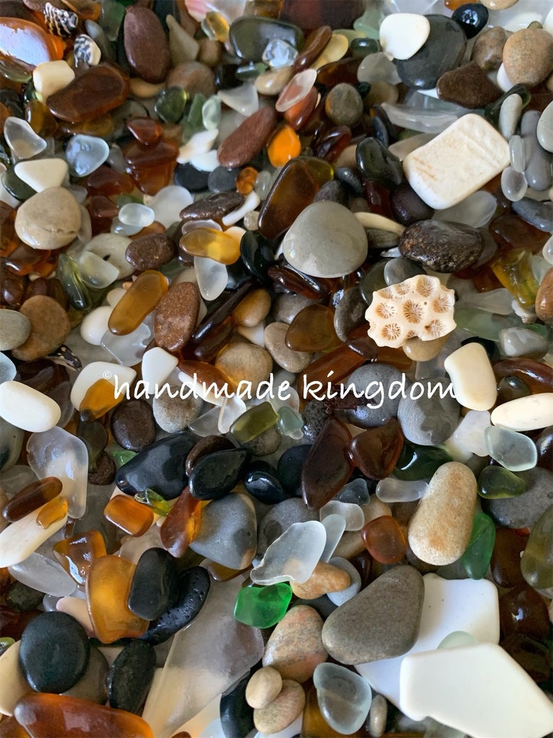 May include: A close-up image of a variety of sea glass and beach pebbles in shades of brown, white, gray, green, and orange. The sea glass is smooth and polished, while the pebbles are rough and textured. The image includes the text "handmade kingdom".