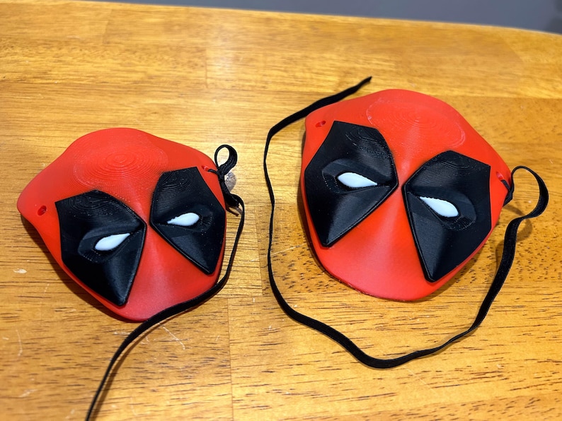 May include: Two red and black Deadpool masks with white eyes. The masks are attached to black elastic straps.