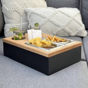 Könnte beinhalten: Ein Holztablett mit schwarzem Sockel und vier Fächern. Das Tablett hat ein Fach für Getränke, ein Fach für Chips, ein Fach für Pommes und ein Fach für Dip. Das Tablett steht auf einem grauen Sofa.