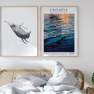 May include: Two framed prints, one with a black and white illustration of a bird with a propeller on its back, and the other with a blue and orange abstract painting of water with the text "CROATIA Tihа voda brege dere. AUGUST 2021 SUNSET SESSION, primo&scaron;ten CROATIA TIMER"