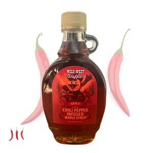 May include: A glass bottle of Wild West Waffles Spicy Chili Pepper Infused Maple Syrup. The label features a cartoon character and the text "Spicy Chili Pepper Infused Maple Syrup". Two pink chili peppers are on either side of the bottle.