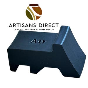 May include: Black ceramic pottery tool with the letters "AD" embossed on the top. The tool is shaped like a small, abstract sculpture.