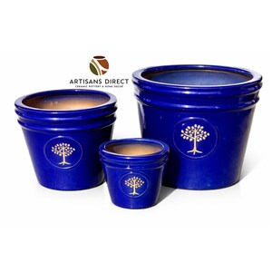 May include: Three cobalt blue ceramic planters of varying sizes. Each planter features a gold tree emblem and a contrasting tan interior. The planters are arranged against a white background, showcasing their glossy finish.