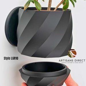 May include: A black, spiral-designed wall-mounted planter with a matching base. The planter holds a green plant with visible leaves. The text "Style LGR10" is visible on the left side of the image. The logo for "ARTISANS DIRECT Ceramic Pottery & Home Decor" is on the right.