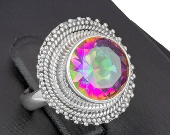May include: A silver ring with a large, round, iridescent gemstone set in a decorative, beaded bezel. The ring is displayed on a black velvet ring display stand.